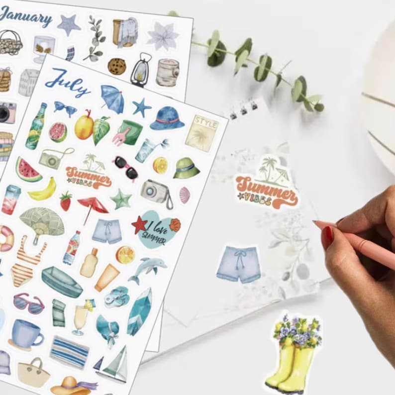 May include: A collection of colorful stickers with summer and seasonal themes. The stickers feature illustrations of fruits, sunglasses, cameras, and other summer-related items. A person is drawing on a notebook with a pink pen.