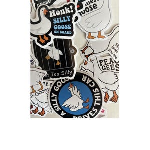 Op de afbeelding: Een verzameling witte ganzenstickers met zwarte contouren en oranje voeten. Sommige stickers hebben tekst als "Honk! Silly Goose On Board" en "Silly Goose Drives This Car". Andere stickers zeggen "Too Silly" en "Pee Gees".