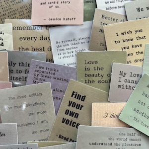 May include: A collection of small, rectangular cards with various quotes and phrases printed on them. The cards are in shades of beige, green, and gray, with black text. Some cards feature quotes, while others have single words.