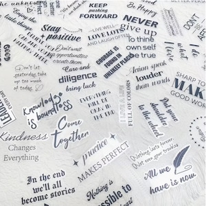 May include: A selection of white stickers featuring inspirational quotes in black lettering. Phrases include "Keep Pushing Forward," "Stay Positive," and "Action speak louder than words." The stickers are on a white surface.