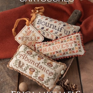 May include: An arrangement of autumn-themed needlepoint cartouches with the words "Autumn Cartouches" at the top. The cartouches feature the words "Bountiful", "Harvest", and "Abundance". The image includes pinecones and small wooden spheres.