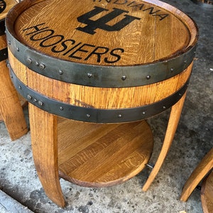 May include: A wooden barrel end table with a black metal band and a top shelf. The table is decorated with the Indiana Hoosiers logo and the words "Indiana Hoosiers".
