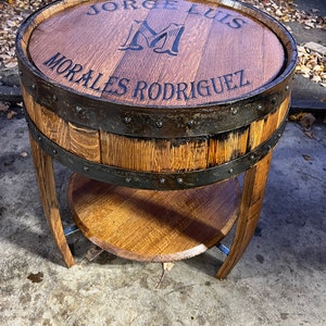 May include: A wooden barrel end table with a metal band and a shelf. The top of the table is engraved with the text "Jorge Luis Morales Rodriguez" and a large "M".