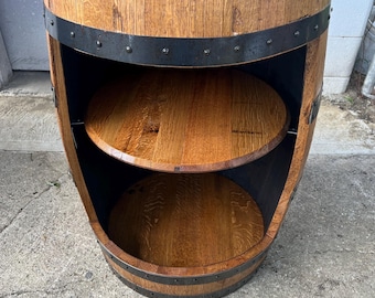 May include: A reclaimed oak barrel, stained dark, with two internal shelves and a top surface. The barrel is secured with dark metal bands and rivets, giving it a rustic, industrial look. The circular shelves are made from the same oak wood as the barrel.