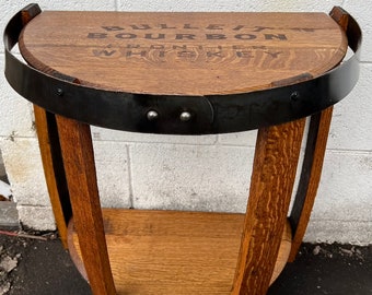 May include: A half-circle wooden side table made from a whiskey barrel. The tabletop features the text "BULLEIT BOURBON FRONTIER WHISKEY". The table has a black metal band around the top and a lower shelf.