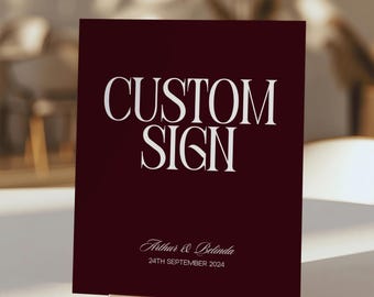 May include: A rectangular dark burgundy sign featuring the white text CUSTOM SIGN in a large serif font. Below, the names Arthur & Belinda are written in a white script font, followed by the date 24TH SEPTEMBER 2024 in a simple white sans-serif font.