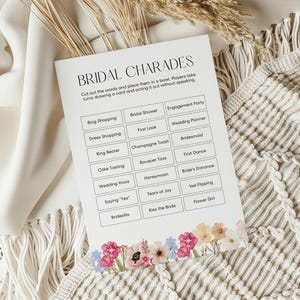Può includere: Una carta di gioco per la festa di addio al nubilato stampabile con sfondo bianco e bordo floreale. La carta ha un titolo che dice "Bridal Charades" e elenca 18 attività legate al matrimonio per gli ospiti da recitare.