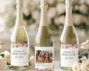 Könnte beinhalten: Drei Champagnerflaschen mit floralen Etiketten. Die Etiketten tragen den Text "Pairs well with bridesmaid duties". Eine Flasche hat ein Foto von zwei Frauen auf dem Etikett.