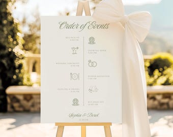 May include: A white rectangular wedding order of events sign on a wooden easel, featuring a large white fabric bow on the right side. The sign displays the text Order of Events, a timeline with icons for bus pick up, cocktail hour, ceremony, dinner, dancing, and bus drop off, plus the names Sophia & Derek and the date 11.20.XX.