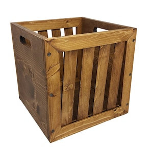 May include: A wooden crate with a dark brown stain. The crate has a slatted front and two cut-out handles on the sides.