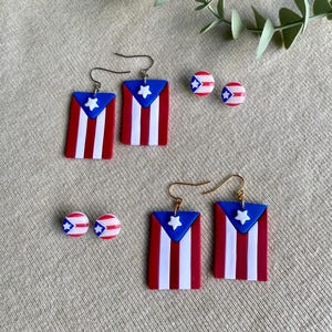 May include: A set of Puerto Rican flag earrings and stud earrings. The dangle earrings feature a red, white, and blue Puerto Rican flag design with a white star. The stud earrings are also red, white, and blue with a white star.