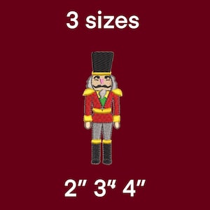 Puede incluir: Un diseño bordado de cascanueces en rojo, dorado y gris, con sombrero y botas negros. El texto "3 tamaños" y las opciones de tamaño de 5 cm, 7.6 cm y 10.2 cm se muestran sobre un fondo burdeos.