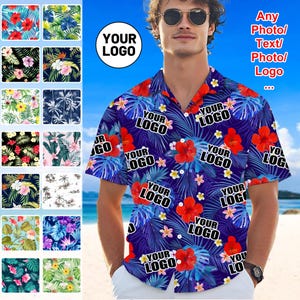 May include: A short-sleeved shirt with a tropical floral design, featuring red hibiscus and blue leaves on a dark blue background. The shirt has the text "YOUR LOGO" overlaid. The shirt is displayed on a person.