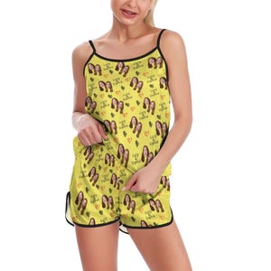 May include: A yellow pajama set consisting of a camisole top and shorts with black trim. The fabric features a repeating pattern of small photographs of two faces, red hearts, and the text "Lucy & Sophia" printed in a dark script font throughout.