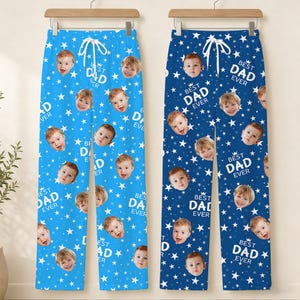 May include: Two pairs of pajama pants, one light blue and one navy blue, both featuring a repeating pattern of baby faces and white stars. The text "BEST DAD EVER" is printed on the pants.