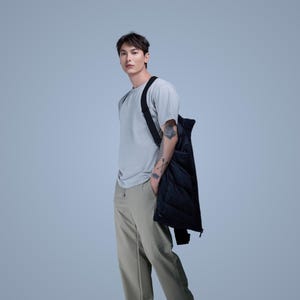 Può includere: Una persona indossa una maglietta grigia e pantaloni kaki, con un gilet nero trapuntato sulla spalla. Il gilet ha una chiusura con cerniera. La persona ha un tatuaggio sul braccio.