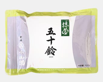 May include: A packaged food product with Japanese text. The packaging is white with a green border and features black and green Japanese characters. The package also includes the text "ISUZU" and "MARUKYU KOYAMAEN". The package contains 100g of product.