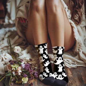 May include: A pair of black socks with a white ghost pattern. The socks are worn on a person's legs.
