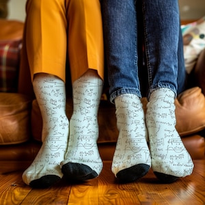 May include: A pair of white socks with black mathematical equations and formulas printed on them. The socks are being worn by two people sitting on a sofa.