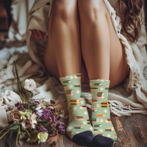 May include: A pair of green socks with a pattern of stacked books and white flowers. The socks are being worn on a person's legs.