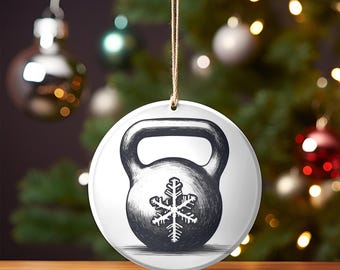 May include: White ceramic Christmas ornament with a black and white illustration of a kettlebell with a snowflake on it.