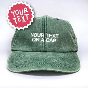 Op de afbeelding: Een groene baseballpet met de tekst "YOUR TEXT ON A CAP" geborduurd in wit op de voorkant.