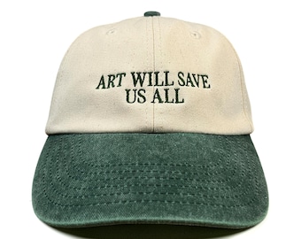 May include: A baseball cap with a cream-colored crown and a dark green brim. The front of the cap features the embroidered text "ART WILL SAVE US ALL" in dark green thread. The cap has a structured front panel and a curved brim with visible stitching.