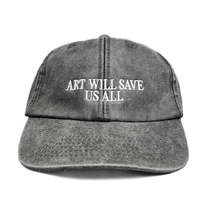 Pode incluir: Um boné de beisebol cinza-carvão com acabamento lavado e desgastado. O painel frontal apresenta o texto bordado em branco "ART WILL SAVE US ALL" em uma fonte sem serifa limpa. O boné tem uma aba curva e uma estrutura de seis painéis.