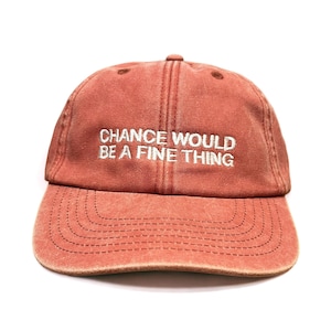 Könnte beinhalten: Eine terrakottafarbene Baseballkappe mit verwaschenem, abgenutztem Finish. Auf der Vorderseite befindet sich ein weißer Stickschriftzug mit dem Text "CHANCE WOULD BE A FINE THING". Die Kappe hat einen gebogenen Schirm mit sichtbaren Ziernähten.