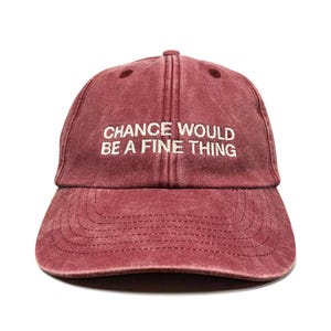 May include: A maroon baseball cap with a washed, vintage-style finish. The front panel features the embroidered white text "CHANCE WOULD BE A FINE THING" in a clean, sans-serif font. The cap has a curved brim and a six-panel construction.