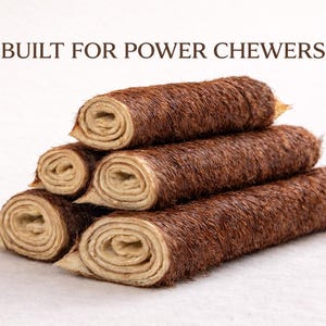 May include: A stack of five brown, rolled dog chews with a furry exterior and a light tan interior. The text "BUILT FOR POWER CHEWERS" is at the top. The chews are arranged on a white surface.