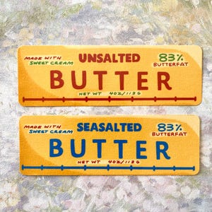 May include: Two yellow butter labels with text. The top label reads "Unsalted Butter" with "83% Butterfat" and "Net Wt 4oz/113g." The bottom label reads "Sea Salted Butter" with the same details.