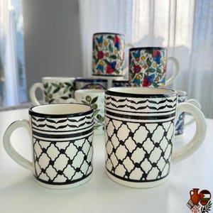 May include: A collection of ceramic mugs with various designs. Some mugs feature floral patterns with red, blue, and yellow flowers. Others have black and white geometric patterns. All mugs have white handles and rims.