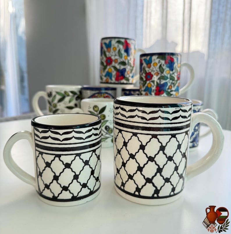 May include: A collection of ceramic mugs with various designs. Some mugs feature floral patterns with red, blue, and yellow flowers. Others have black and white geometric patterns. All mugs have white handles and rims.