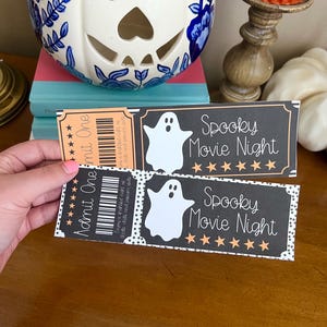 K&ouml;nnte beinhalten: Zwei schwarze und orangefarbene druckbare Halloween-Kinotickets mit einer Geistergrafik und dem Text "Spooky Movie Night" und f&uuml;nf goldenen Sternen.