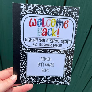 Puede incluir: Una tarjeta de estilo cuaderno en blanco y negro con el texto "WELCOME Back! Wishing you a great year! Love, The Stevens family" y un espacio para adjuntar una tarjeta de regalo.