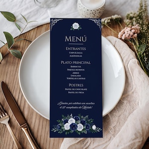 May include: A vertical rectangular menu card with a dark navy blue background, featuring white floral illustrations at the top and bottom. The text includes "MENÚ", "ENTRANTES", "PLATO PRINCIPAL", "POSTRES", and "¡Gracias por celebrar con nosotras el 15 cumpleaños de Mariah!".