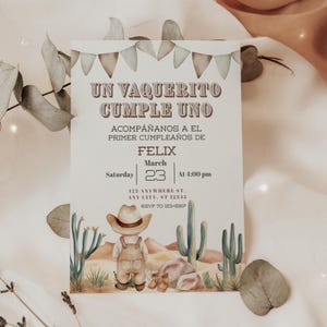 May include: A rectangular birthday invitation card featuring a watercolour illustration of a child in a cowboy hat and overalls standing in a desert with cacti. The text reads UN VAQUERITO CUMPLE UNO, ACOMPAÑANOS A EL PRIMER CUMPLEAÑOS DE FELIX, March 23, 4:00 pm.