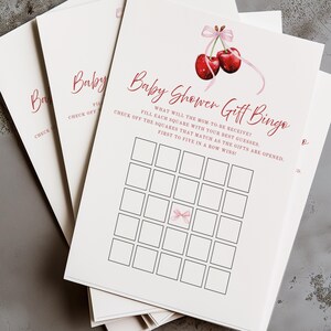 Op de afbeelding: Een printbare baby shower cadeau bingo kaart met een roze strik en twee rode kersen. De kaart heeft 25 vakjes die gasten kunnen afvinken terwijl de cadeaus worden geopend. De tekst luidt: "Wat krijgt de aanstaande moeder? Vul elk vakje in met je beste gok. Vink de vakjes aan die overeenkomen terwijl de cadeaus worden geopend. De eerste die vijf op een rij heeft, wint!"
