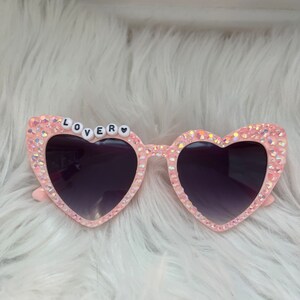 May include: Pink heart-shaped sunglasses with rhinestones and the word "LOVER" spelled out in black letters on the frame.