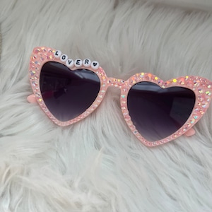 May include: Pink heart-shaped sunglasses with rhinestones and the word "LOVER" spelled out in white beads.