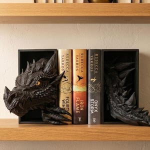 May include: Black dragon bookends featuring a detailed head and tail design. The bookends hold three books titled "Fourth Wing", "Iron Flame", and "Onyx Storm" by Rebecca Yarros. The bookends are on a wooden shelf.