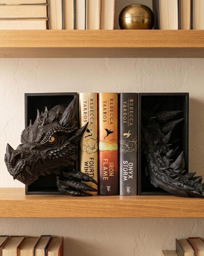 May include: Black dragon bookends featuring a detailed head and tail design. The bookends hold three books titled "Fourth Wing", "Iron Flame", and "Onyx Storm" by Rebecca Yarros. The bookends are on a wooden shelf.