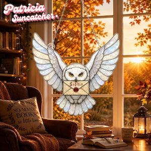 May include: A stained glass suncatcher shaped like a white owl with spread wings, holding an envelope in its talons. The envelope features the name Sophia written in red script with a red wax seal. The owl has yellow eyes and is suspended by chains.