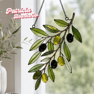 Könnte beinhalten: Ein Glasmalerei-Olivenzweig mit grünen Blättern und schwarzen und gelben Oliven, der an einer Kette hängt. Der Text "Patricia Bourke Co" ist oben links zu sehen.