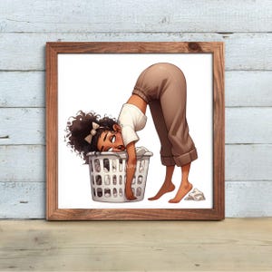 May include: A framed print featuring an illustration of a person leaning over a laundry basket. The person is wearing a white shirt and brown pants. The laundry basket is white and filled with clothes. The artwork is set against a light wood background.