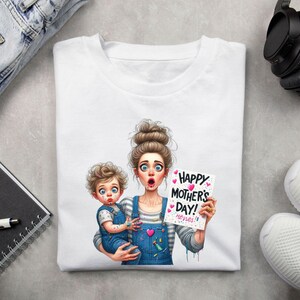 May include: White t-shirt with a colorful illustration of a mother and child. The mother is holding the child and both are covered in paint. The child is holding a sign that says "Happy Mother's Day! Heroes!"