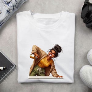 Puede incluir: Camiseta blanca con una ilustraci&oacute;n de dibujos animados de una mujer sosteniendo un tarro. La mujer lleva una camiseta amarilla, pantalones verde oliva y una rebeca color canela. Su expresi&oacute;n es de frustraci&oacute;n. La camiseta es de cuello redondo.