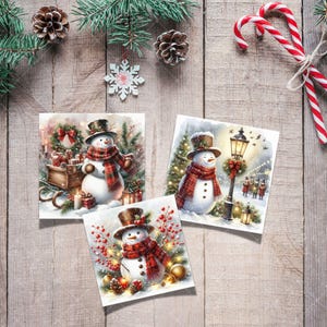 May include: Three square Christmas cards featuring watercolor snowmen wearing top hats and plaid scarves. The cards are decorated with festive scenes, including gifts, a lamppost, and holiday greenery. The cards are arranged on a wooden surface with pinecones and candy canes.