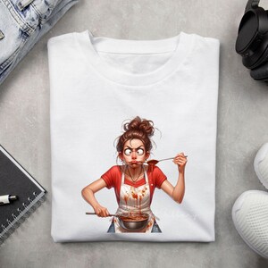 May include: White t-shirt featuring a cartoon illustration of a woman tasting food from a pot. The woman wears a red shirt, a white apron with sauce stains, and has a surprised expression. The image is a humorous depiction of cooking.